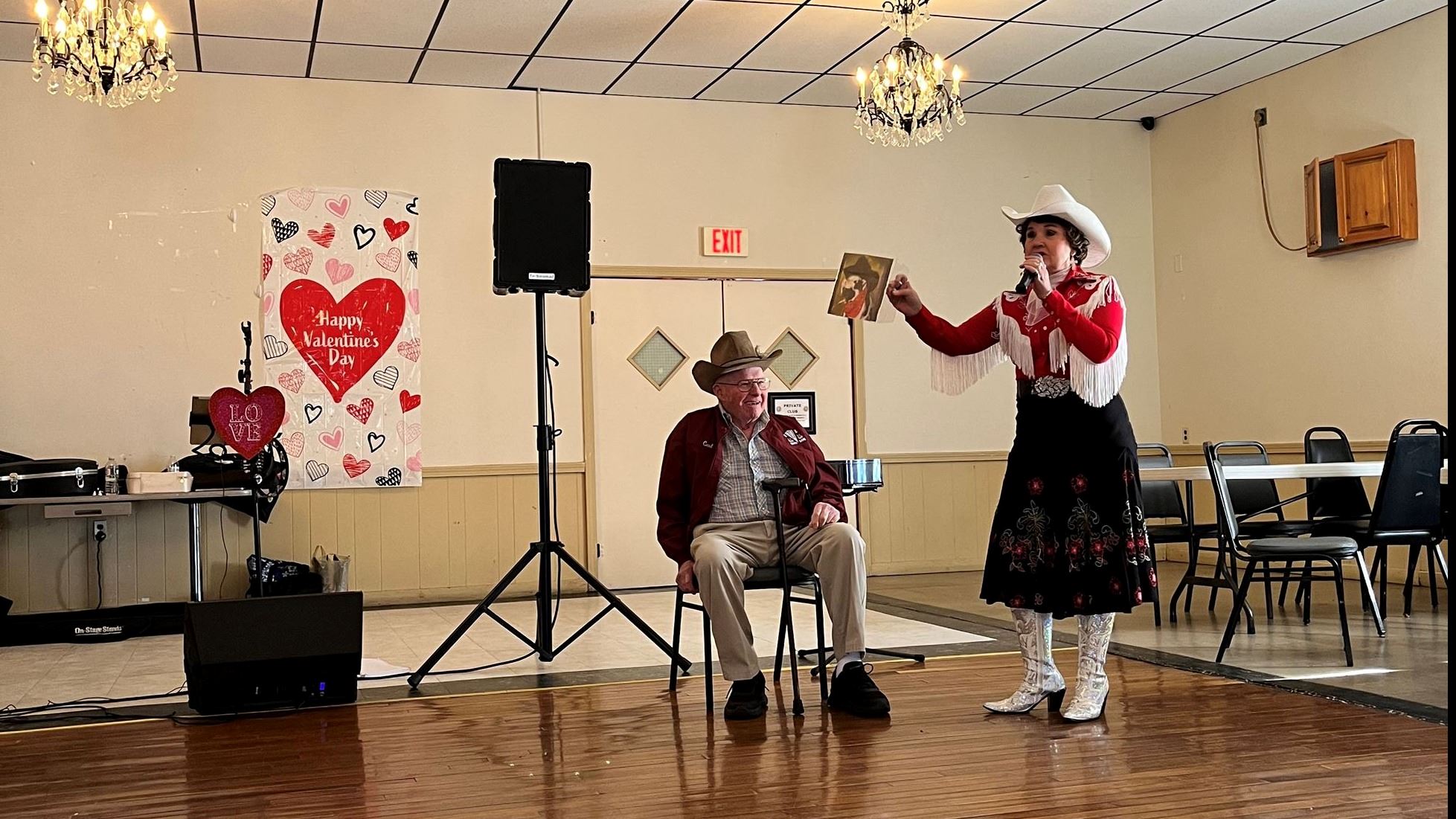 A man sitting in a chair and a woman standing with a microphone