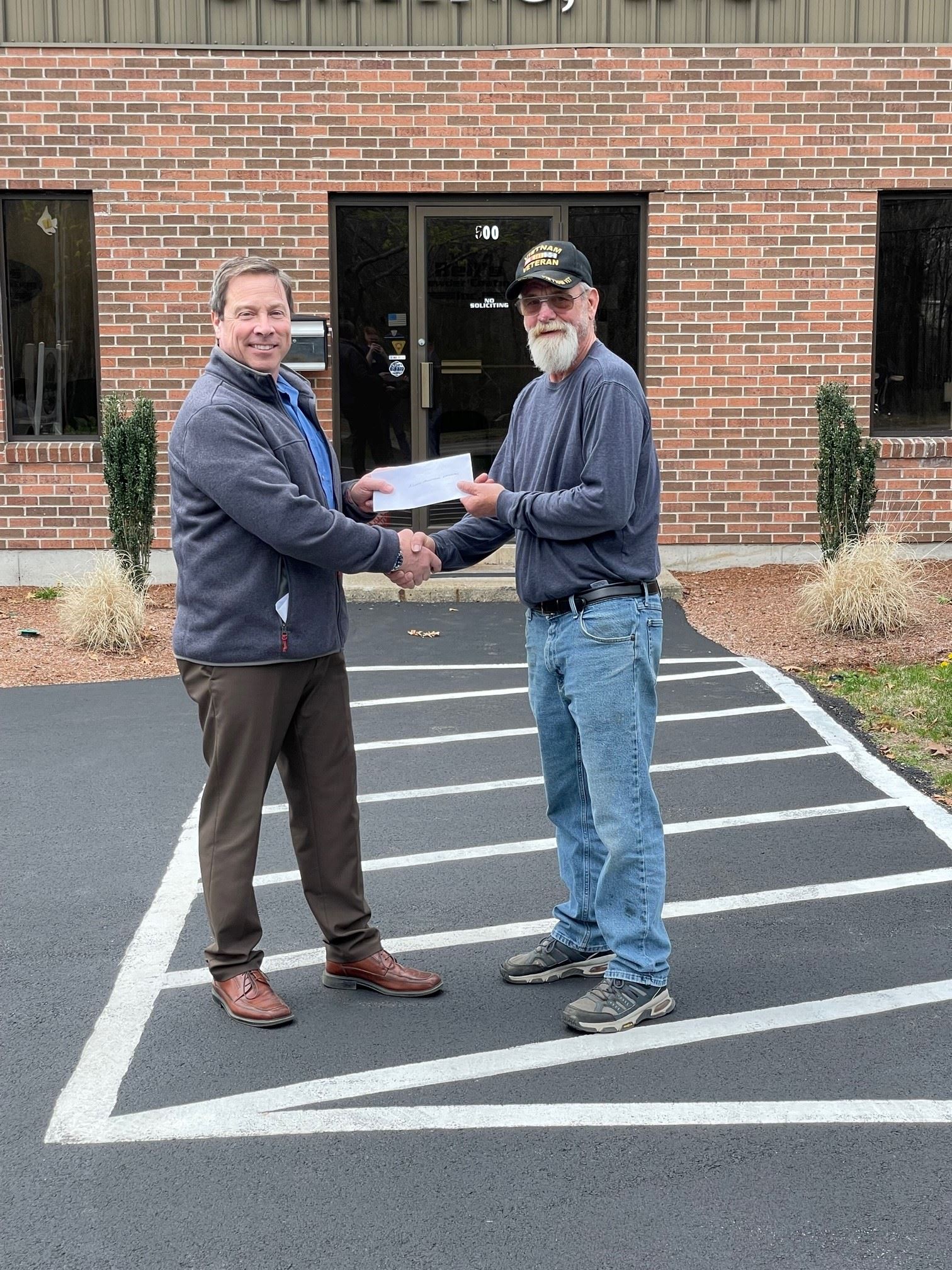 Two men shaking hands and holding a check between them